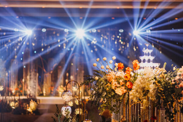 Floral wedding décor with glowing candles and crystal strands, under bright stage lights and sparkling backdrop at a reception venue